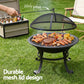 Outdoor grill with mesh lid on a grassy area, surrounded by a cooler and chairs.