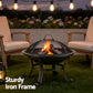 Fire pit with burning wood surrounded by two chairs and string lights in a garden setting.