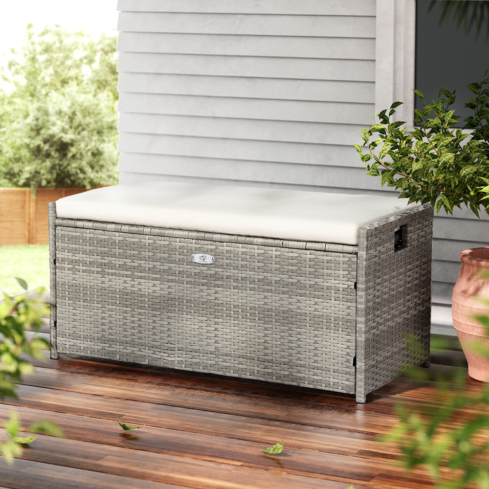 Outdoor storage box with cushion on a wooden deck, surrounded by plants.