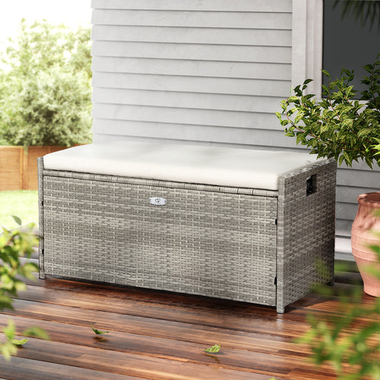 Outdoor storage box with cushion on a wooden deck, surrounded by plants.