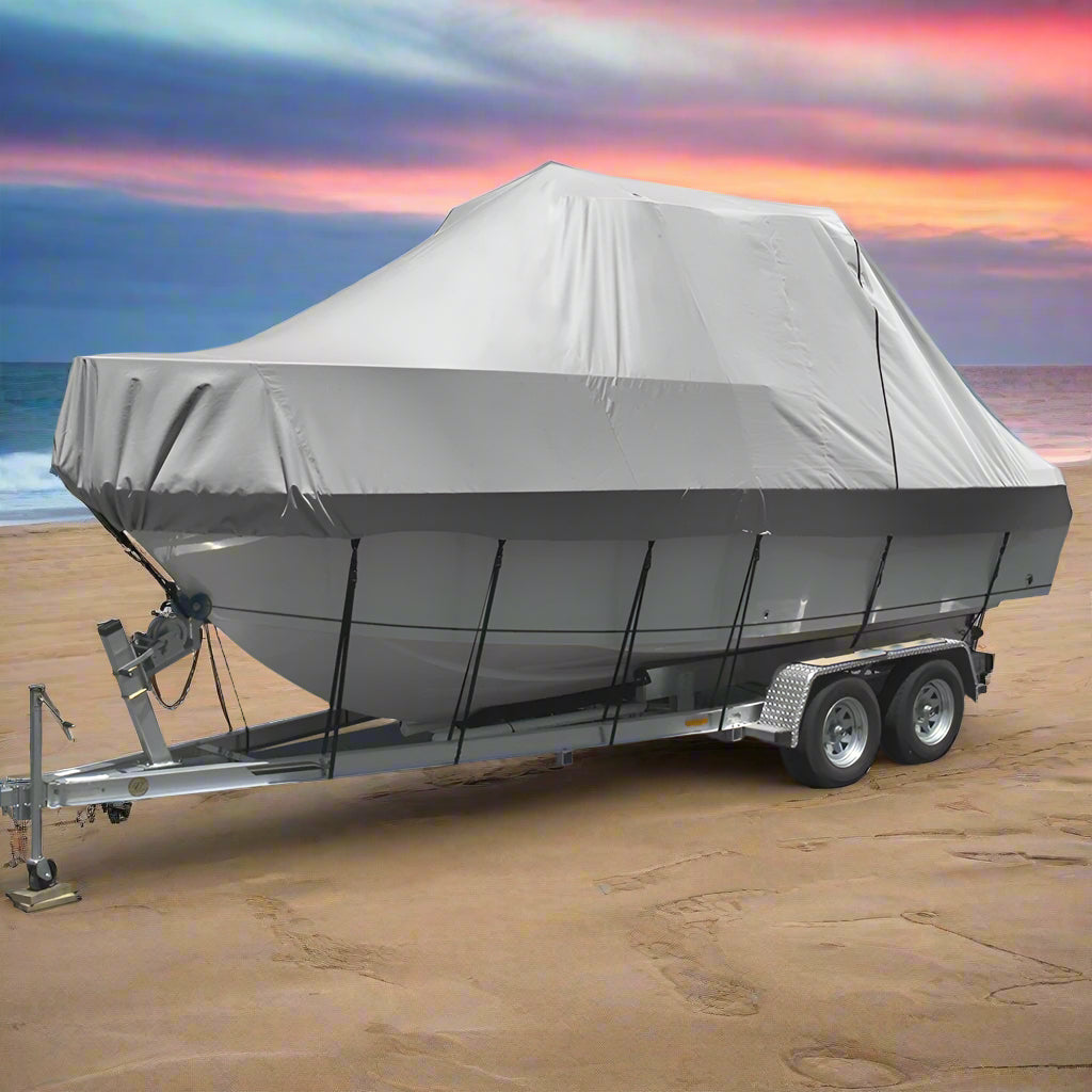 Boat on a trailer with a gray cover on a sandy beach with ocean in the background