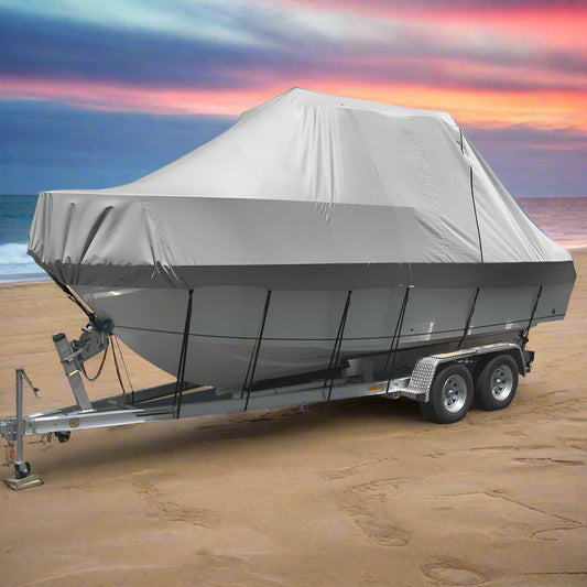 Boat on a trailer with a gray cover on a sandy beach with ocean in the background