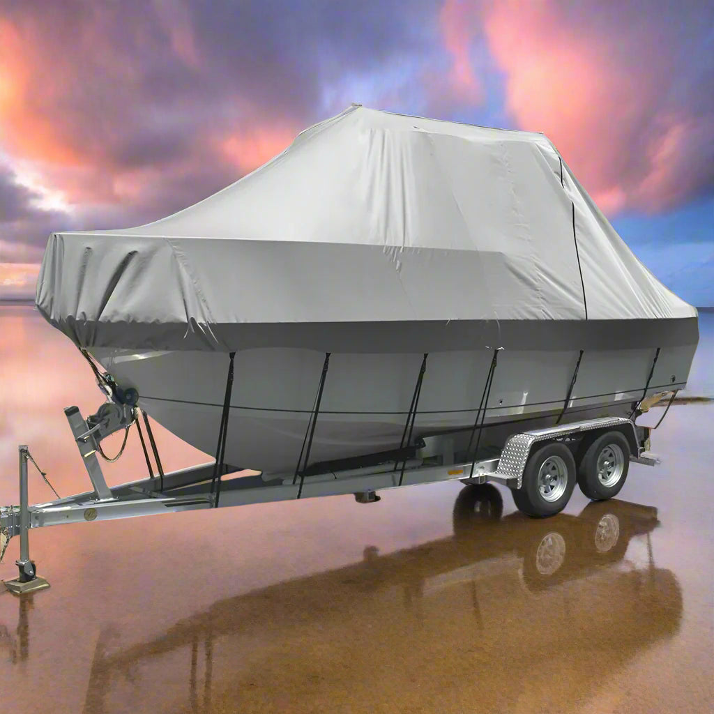 Boat on a trailer with a gray cover on a sandy beach with ocean in the background