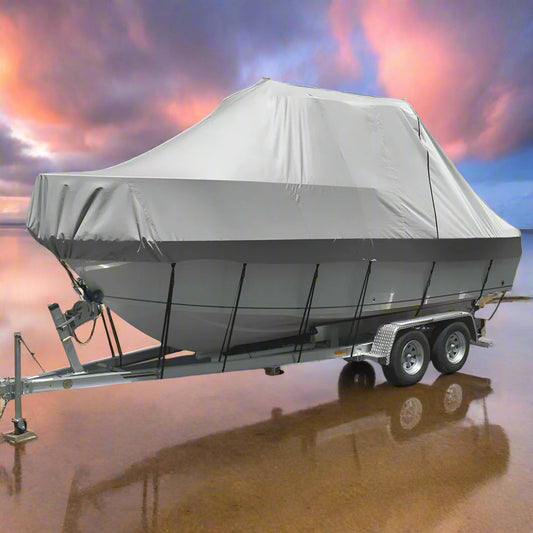 Boat on a trailer with a gray cover on a sandy beach with ocean in the background