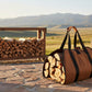 Brown duffel bag with black straps filled with wood, held by a person wearing jeans and sneakers.